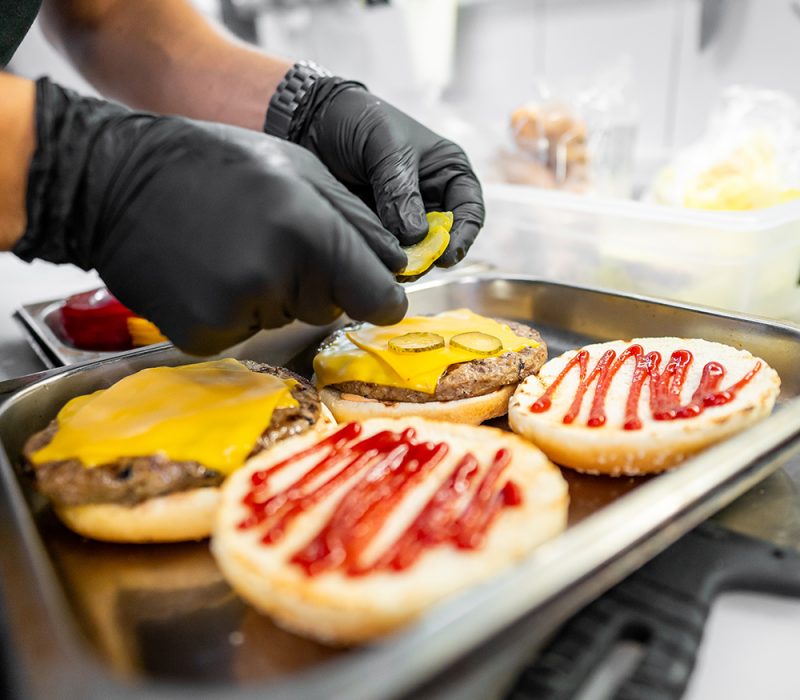 A close-up of hands preparing hamburgers with cheese and condime